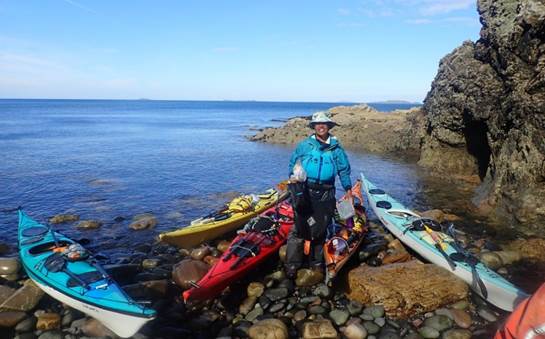 A person standing next to kayaks on a rocky beach

Description automatically generated with medium confidence