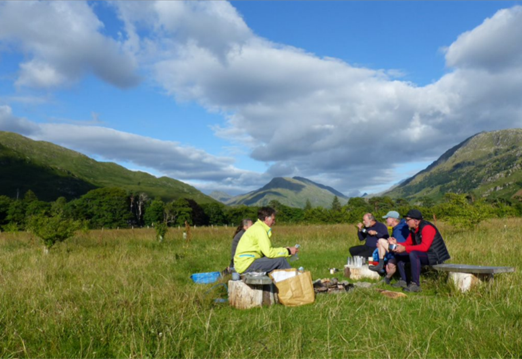 A group of people sitting around a table in a field

Description automatically generated