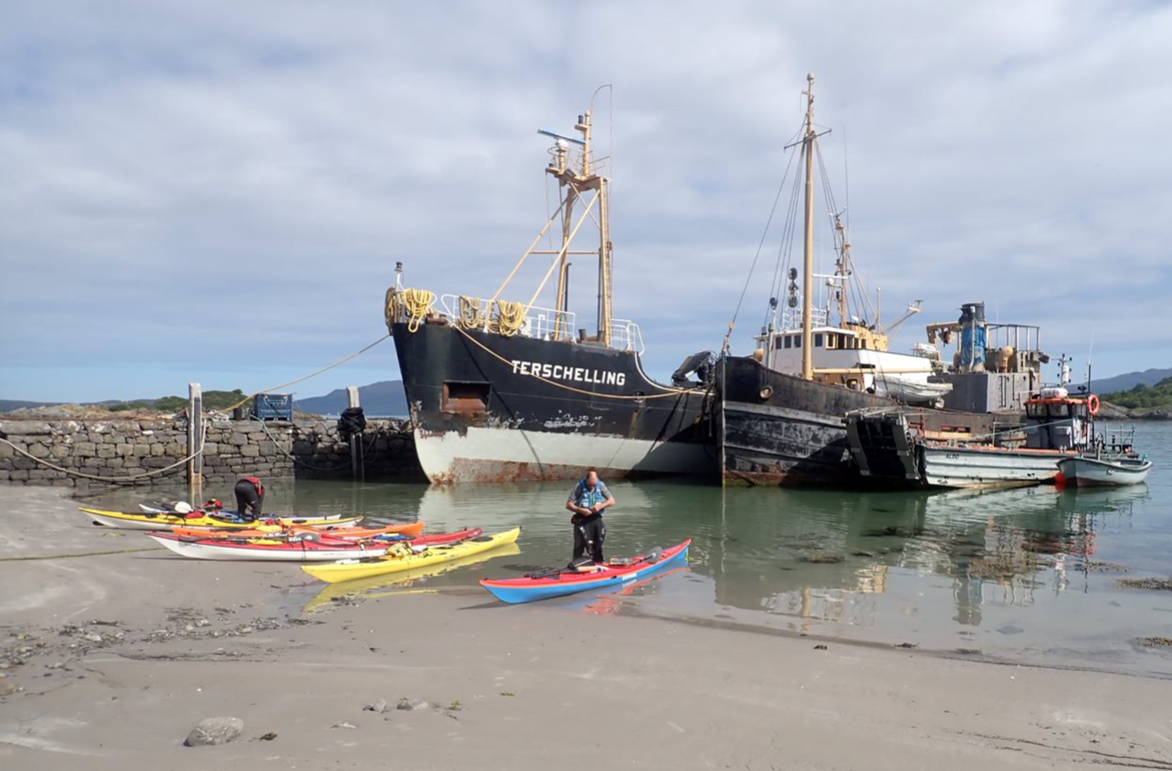 A person standing in a kayak next to a boat

Description automatically generated