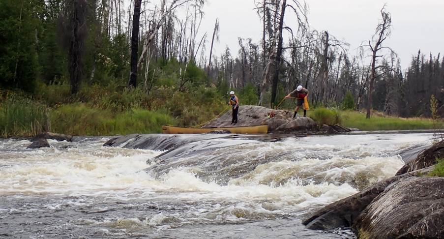 A group of people standing on a rock in a river

Description automatically generated