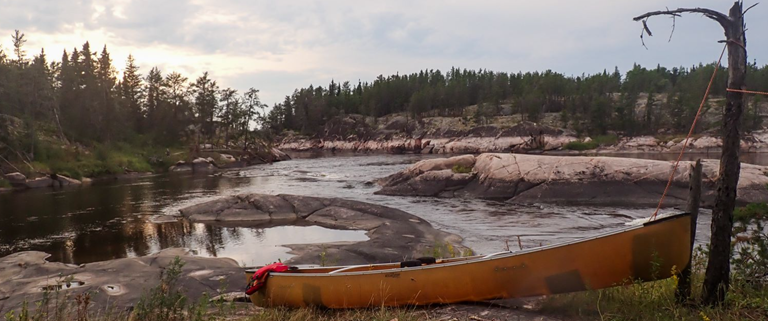 A canoe on the shore of a river

Description automatically generated