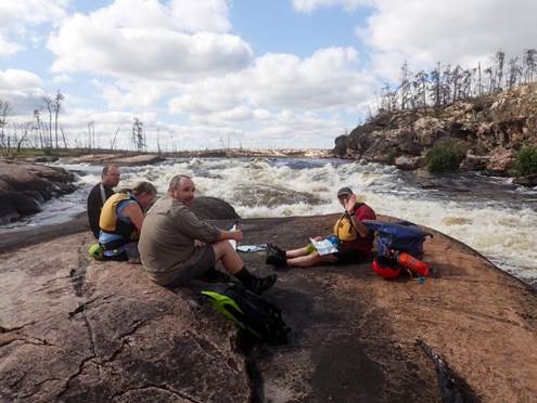 A group of people sitting on a rock by a river

Description automatically generated