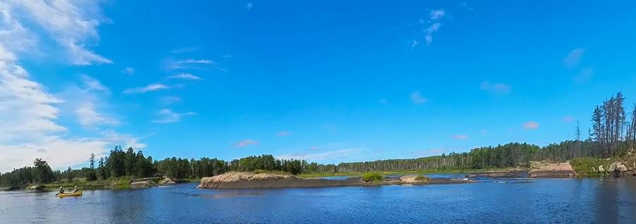 A body of water with trees and a blue sky

Description automatically generated