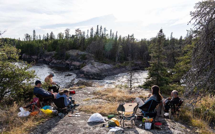 A group of people sitting on a rocky shore by a river

Description automatically generated