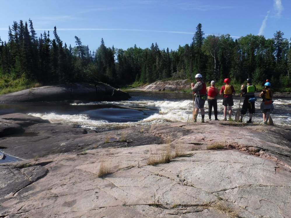 A group of people standing on a rocky shore

Description automatically generated