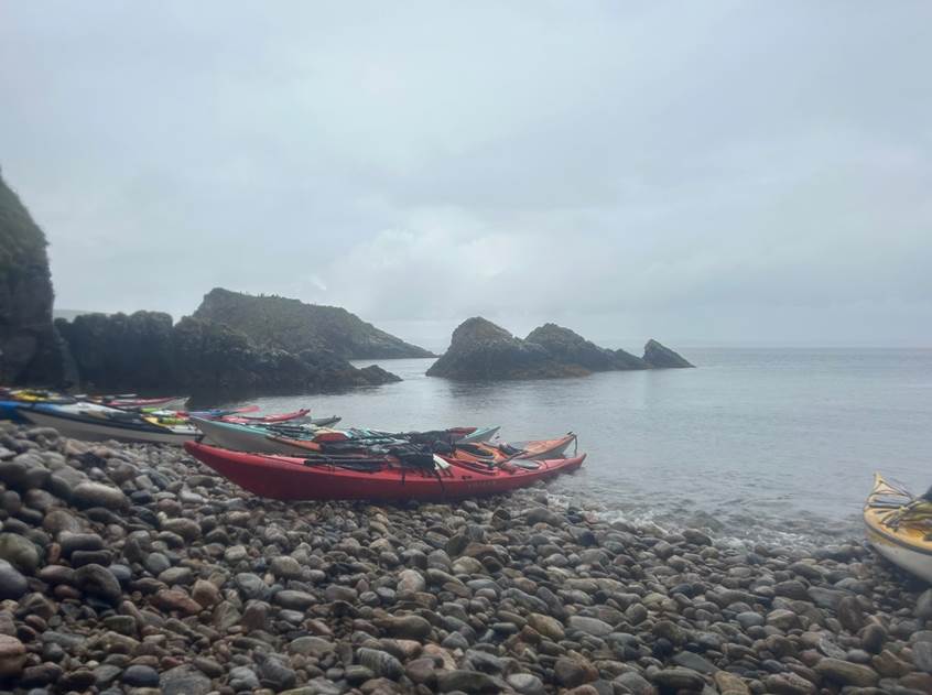 A group of kayaks on a rocky beach

Description automatically generated