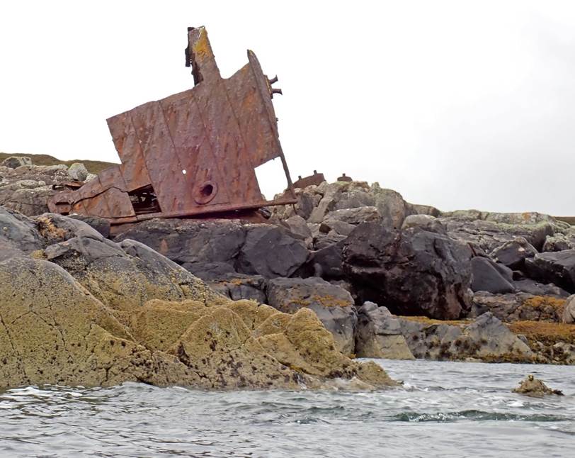 A rusty ship on rocks by water

Description automatically generated