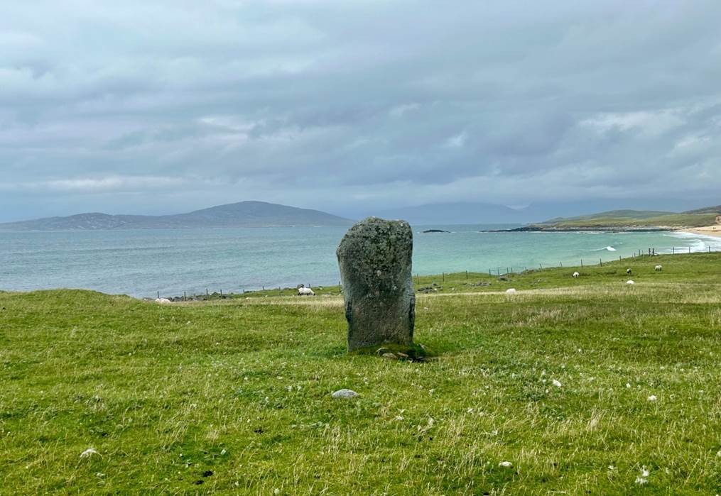 A stone in a grassy field by the water

Description automatically generated