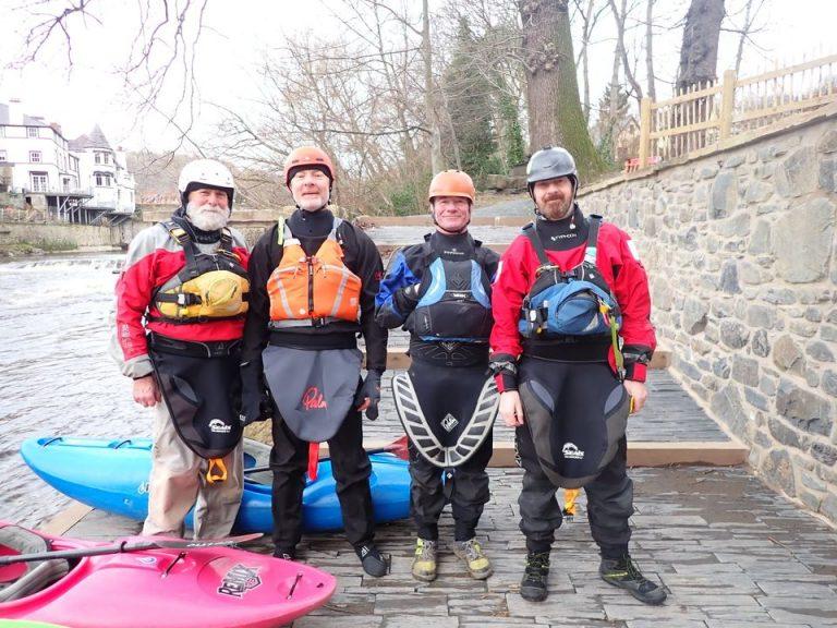 A group of people wearing life jackets and standing next to a kayak Description automatically generated with medium confidence