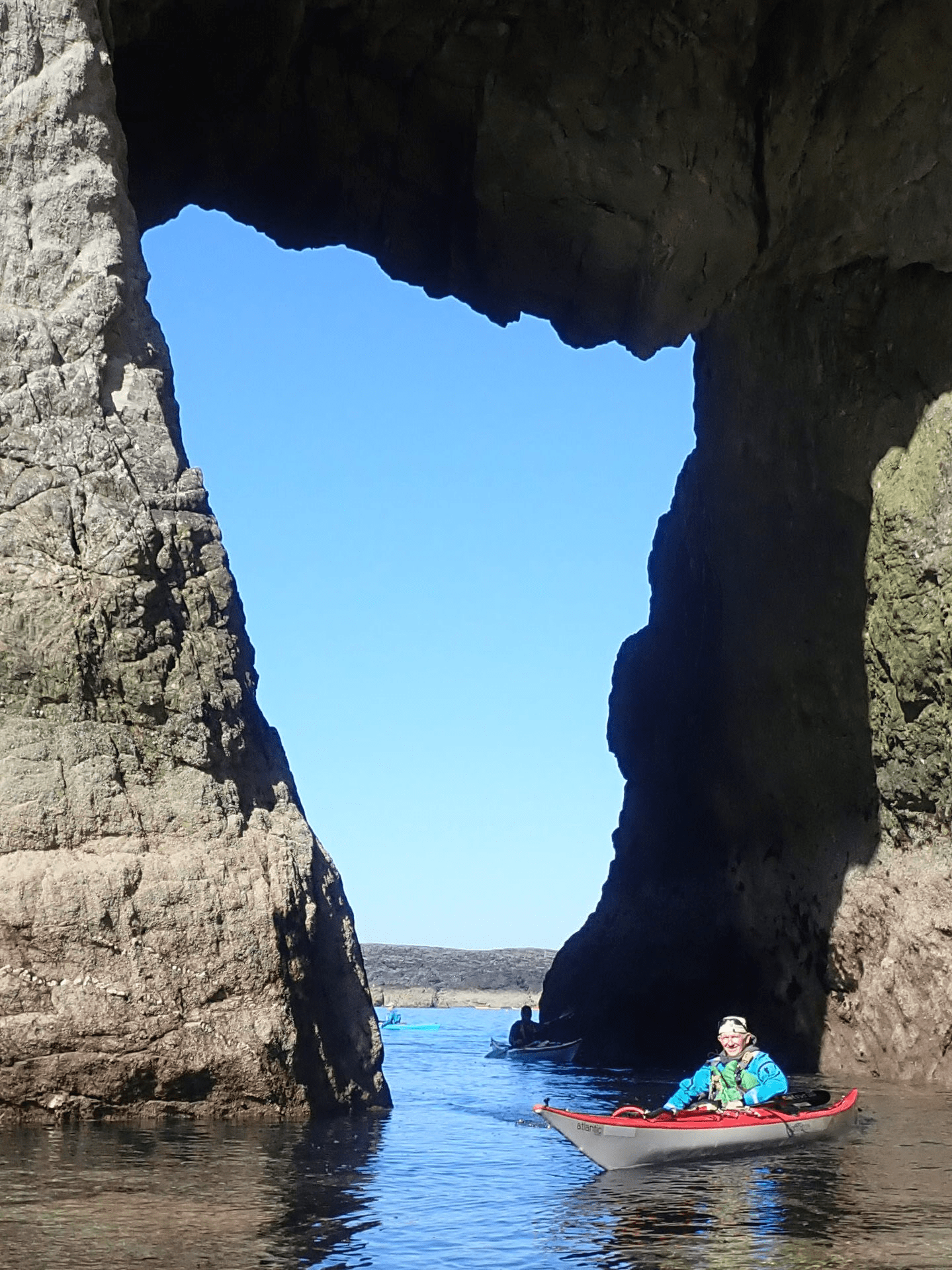 A person in a boat in a body of water between large rocksDescription automatically generated with low confidence