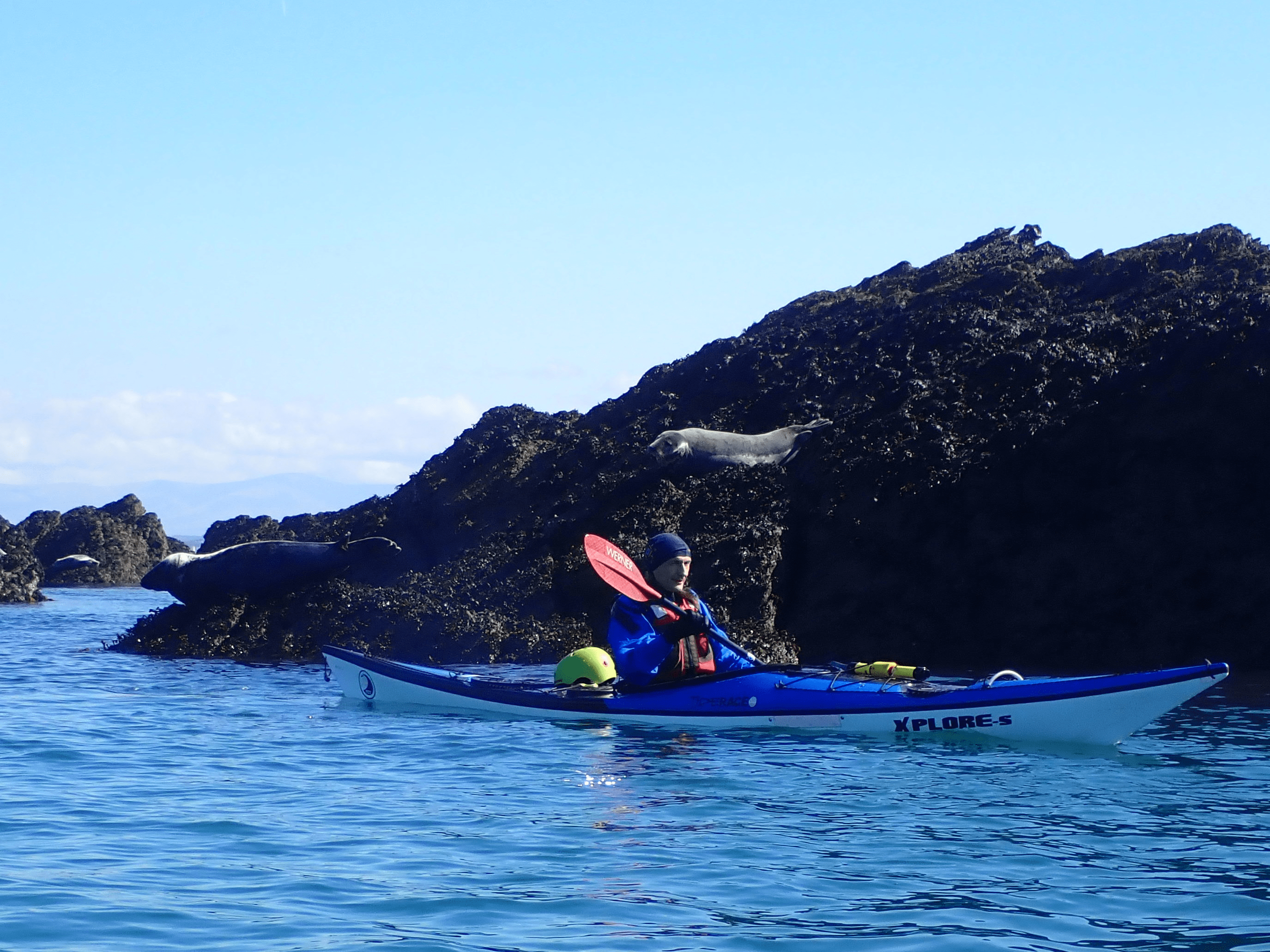 A person in a kayak in the water with a mountain in the backgroundDescription automatically generated with low confidence