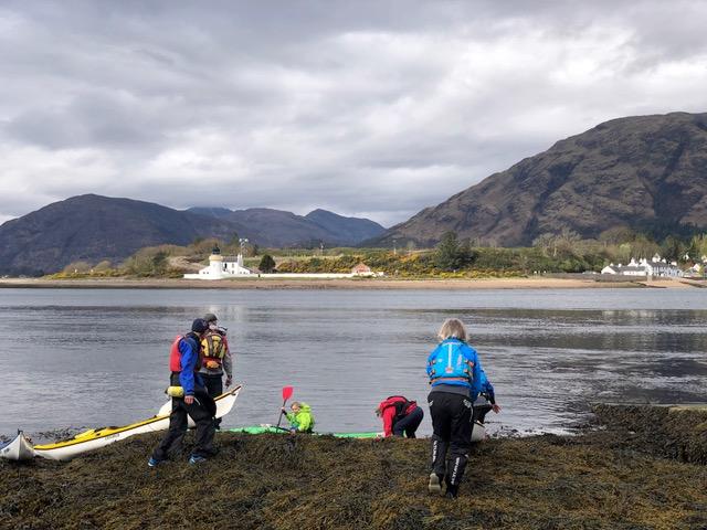 A group of people standing next to a body of water with a boat in itDescription automatically generated with low confidence