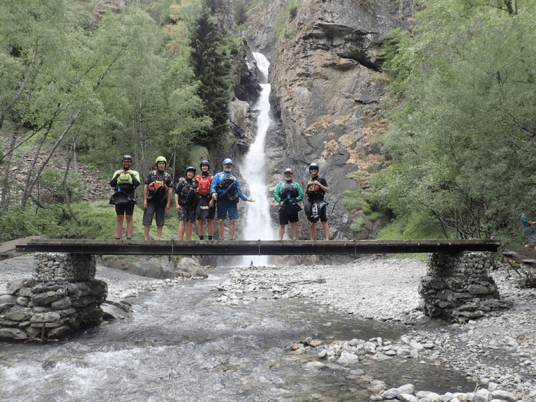 A group of people standing on a bridge over a river with a waterfall Description automatically generated with medium confidence