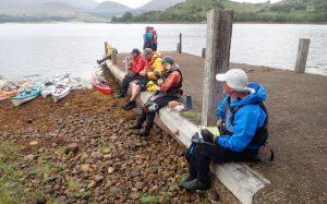 A group of people sitting on a bench by a body of water Description automatically generated with medium confidence