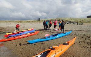 A group of people standing next to kayaks on a beach Description automatically generated with medium confidence
