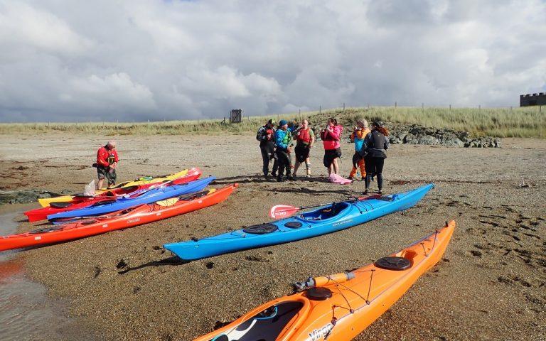 A group of people standing next to kayaks on a beach Description automatically generated with medium confidence