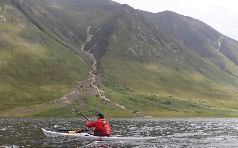 A person in a kayak in a river between mountainsDescription automatically generated with medium confidence