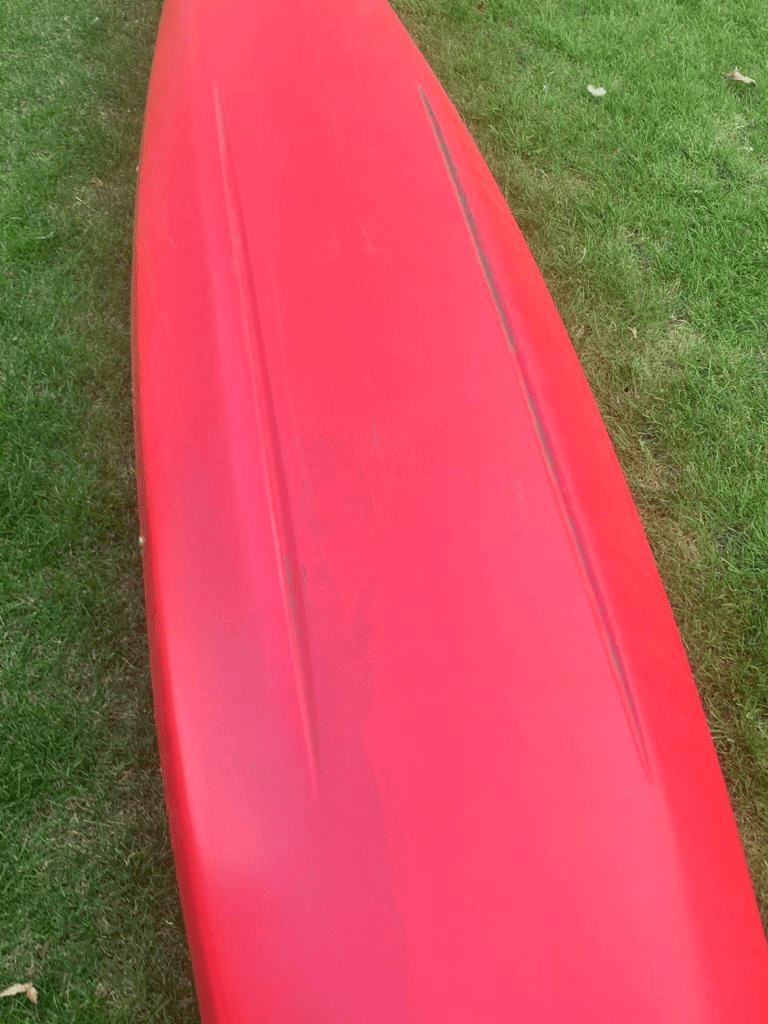 A red surfboard on grassDescription automatically generated with low confidence