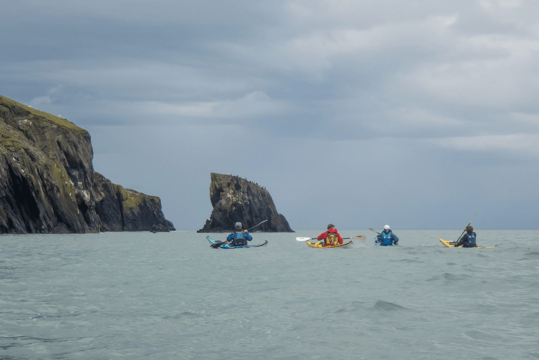 A group of people in kayaks in the water by large rocksDescription automatically generated with low confidence