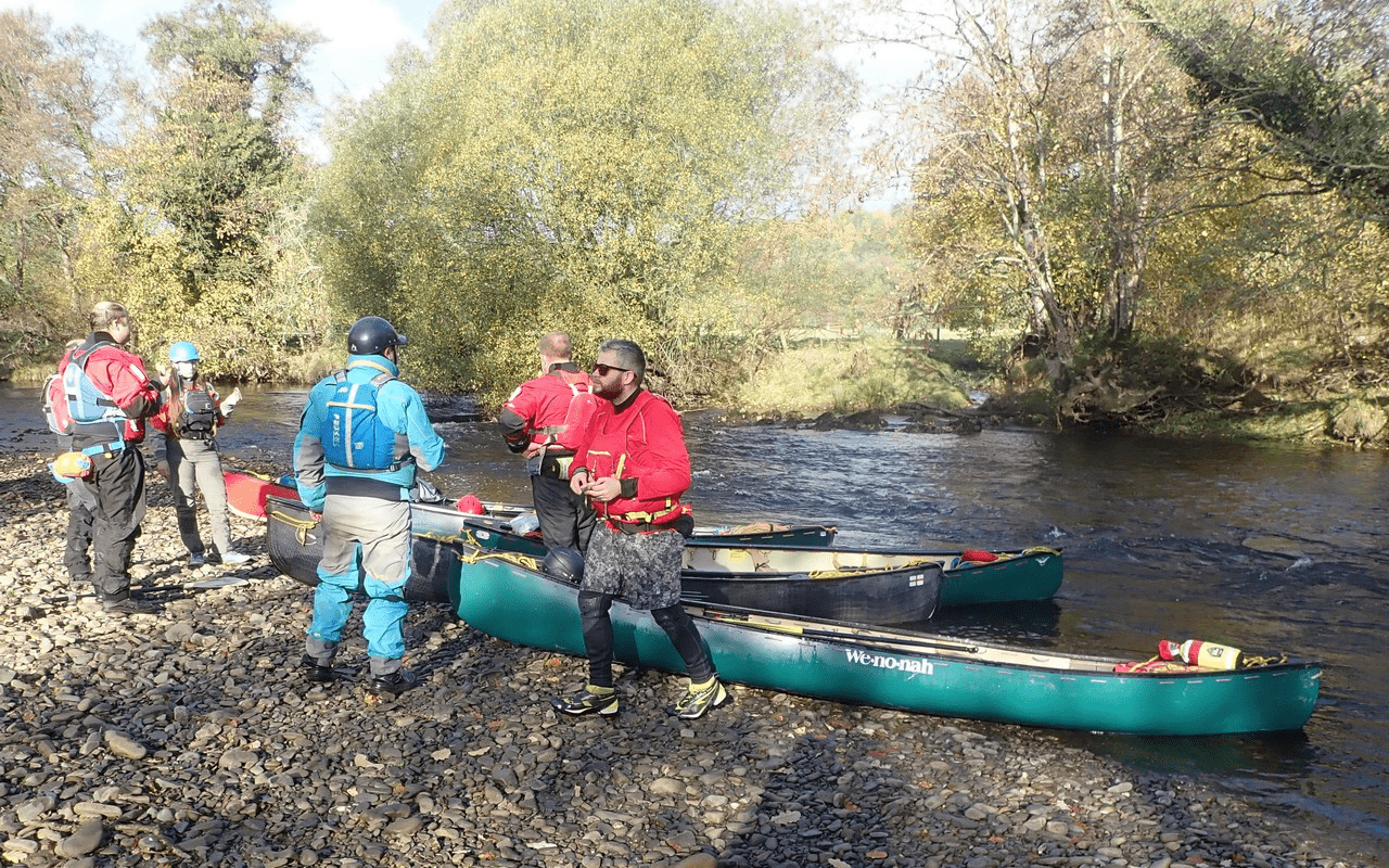 A group of people standing next to canoes on a riverDescription automatically generated with medium confidence