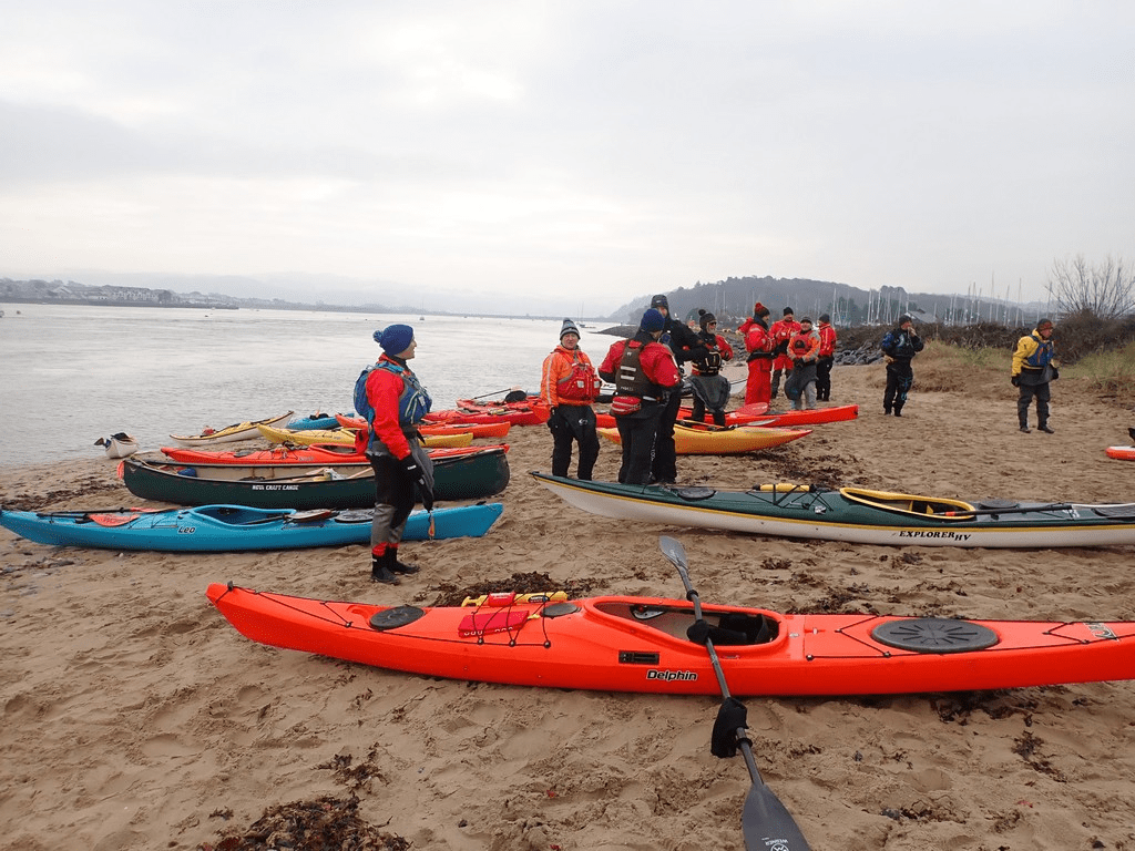 A group of people standing next to kayaks on a beachDescription automatically generated with medium confidence