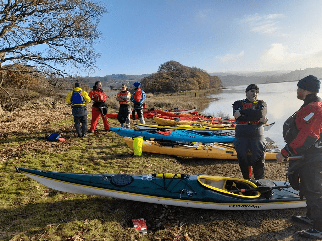 A group of people standing next to kayaks on a beachDescription automatically generated with medium confidence