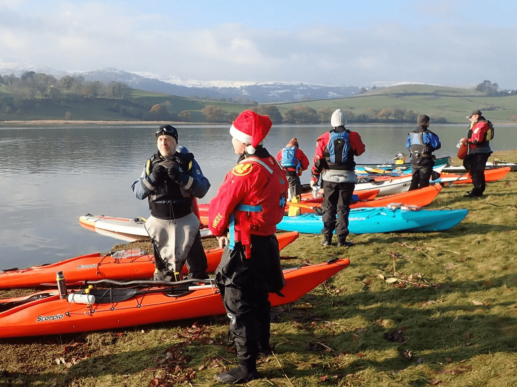 A group of people standing next to kayaks on a lakeDescription automatically generated with low confidence