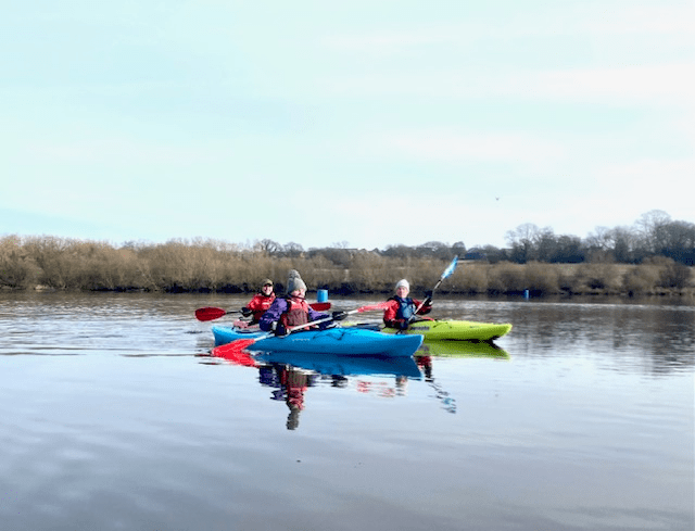 A group of people in a row boat on a lakeDescription automatically generated with low confidence