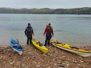 A group of people standing next to kayaks on a beach Description automatically generated with low confidence
