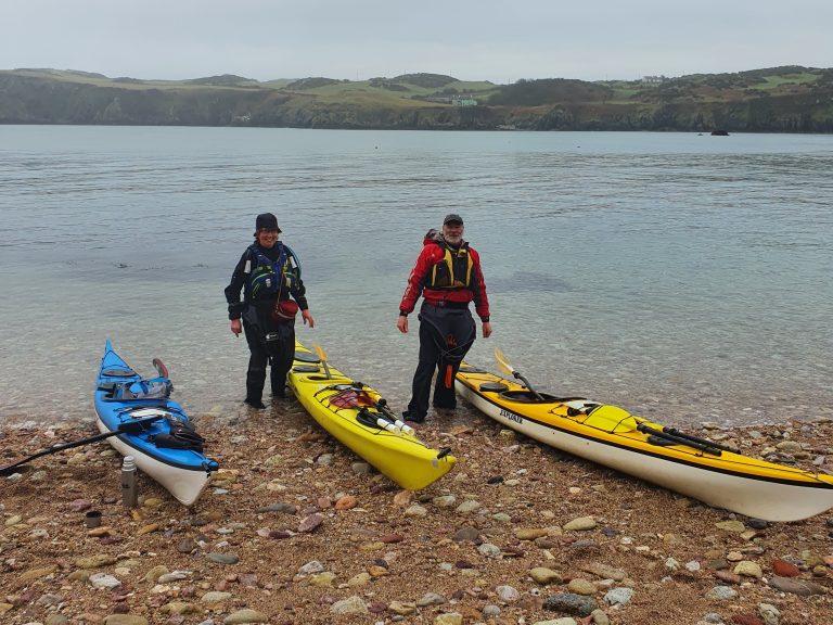 A group of people standing next to kayaks on a beach Description automatically generated with low confidence