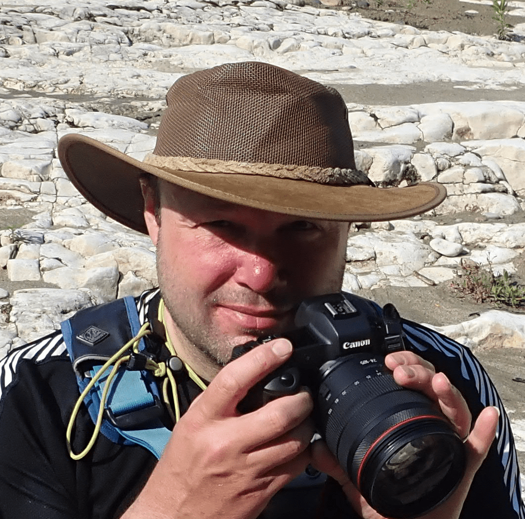 A person wearing a hat and holding a cameraDescription automatically generated