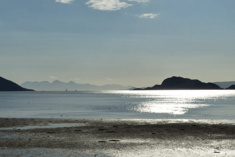 A beach with a body of water and mountains in the backgroundDescription automatically generated