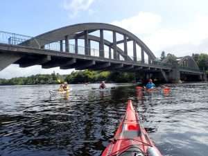 A group of people kayaking under a bridge Description automatically generated