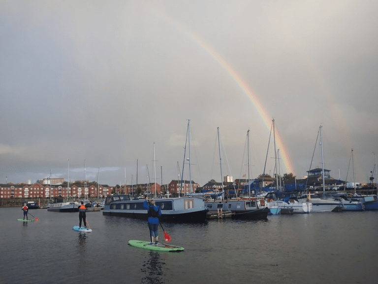 A rainbow over a body of water with boats and people on it Description automatically generated