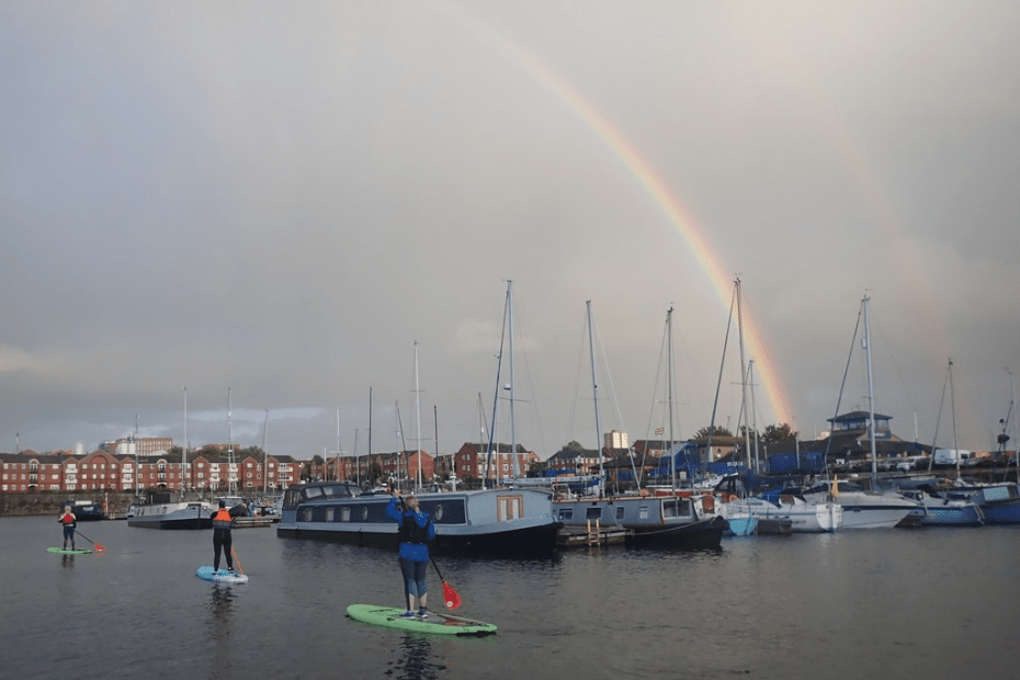 A rainbow over a body of water with boats and people on it Description automatically generated