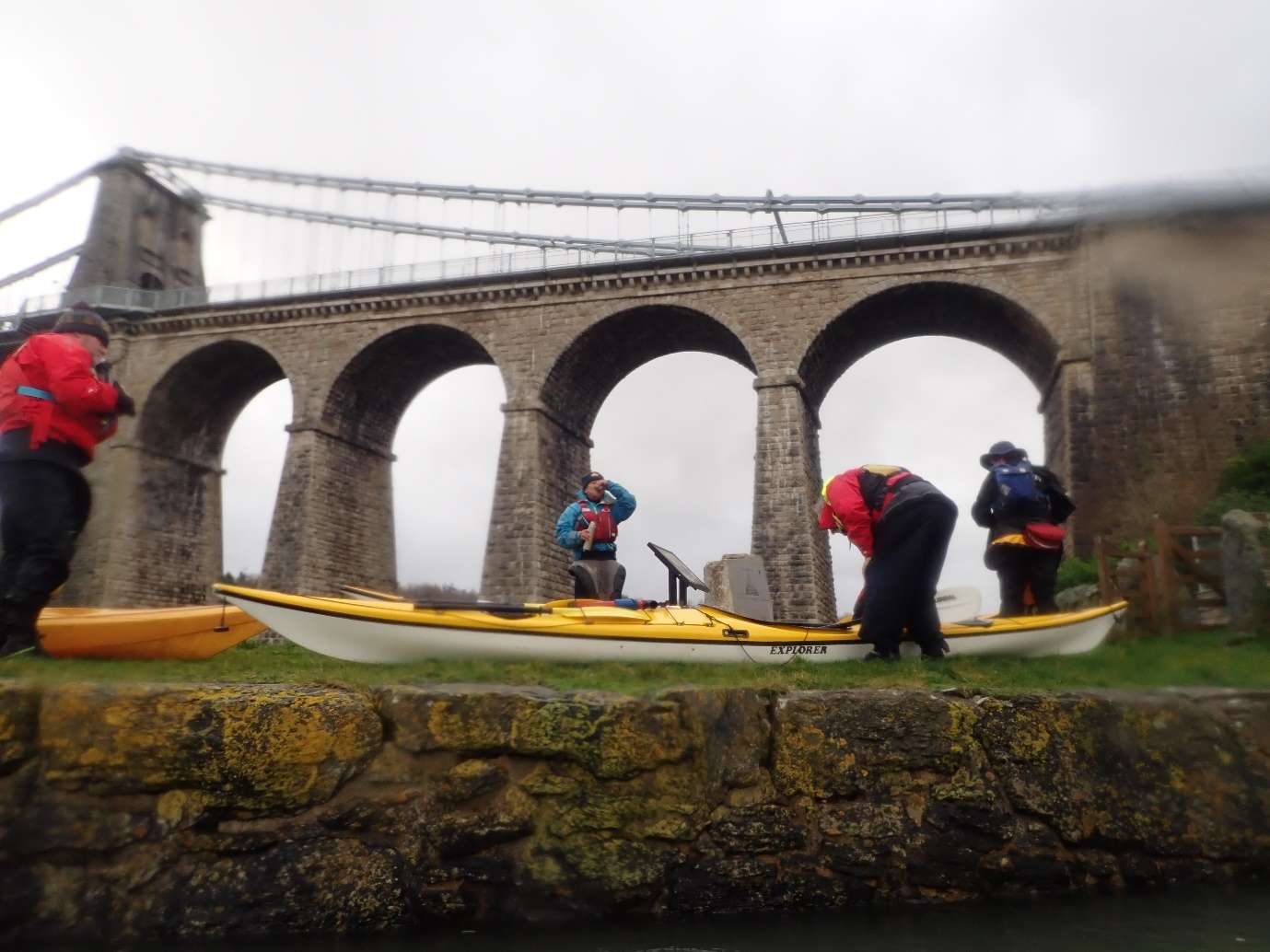 People standing on a rock near a bridgeDescription automatically generated