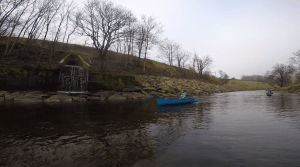 A person in a blue canoe on a river Description automatically generated
