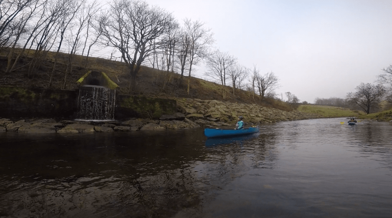 A person in a blue canoe on a river Description automatically generated