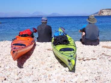 A group of people sitting on the beach with kayaks

Description automatically generated