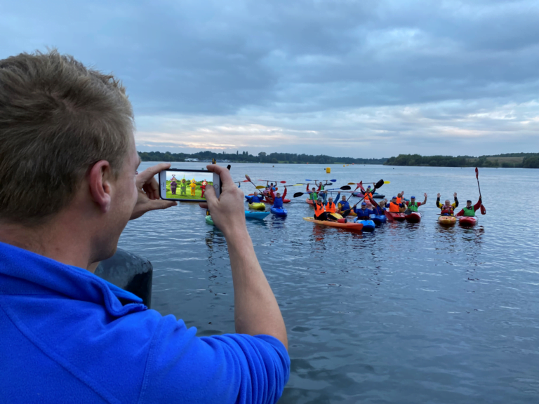 A person taking a picture of a group of kayaks Description automatically generated