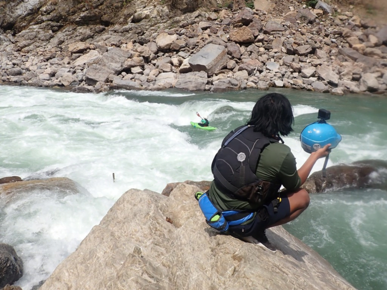 A person sitting on a rock by a river Description automatically generated