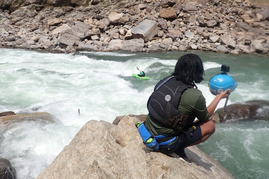 A person sitting on a rock by a river Description automatically generated