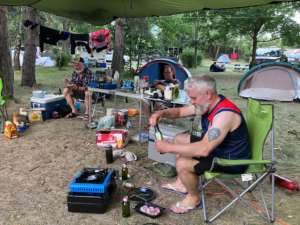 A group of men sitting outside by a table with food and drinks Description automatically generated