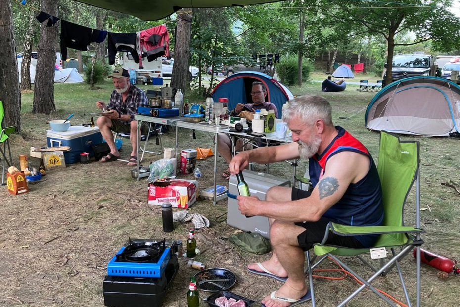 A group of men sitting outside by a table with food and drinks Description automatically generated