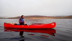 A person in a red canoe on a lake Description automatically generated