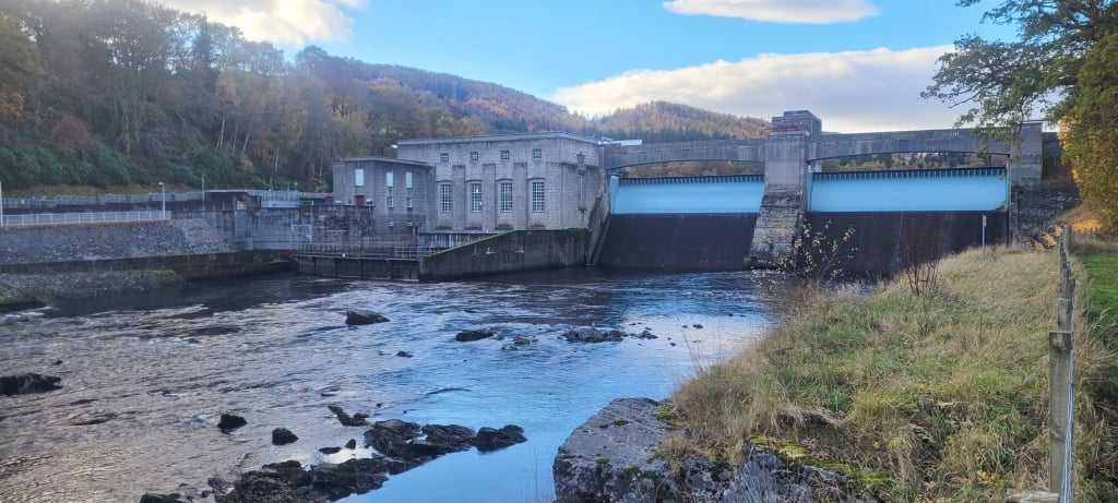 A water dam with a building and a riverDescription automatically generated with medium confidence