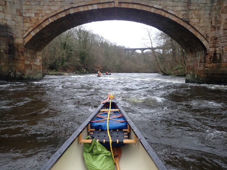 Canoeing under stone bridge on scenic river