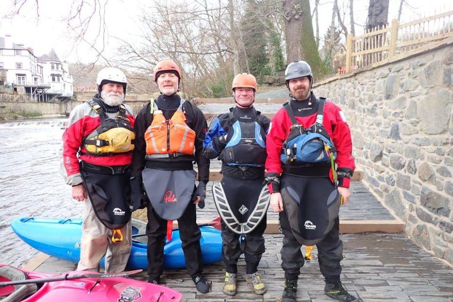A group of people wearing life jackets and standing next to a kayak Description automatically generated with medium confidence