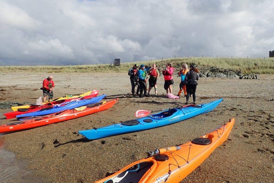 A group of people standing next to kayaks on a beach Description automatically generated with medium confidence