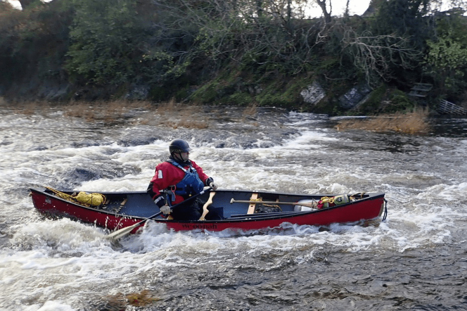 A person in a red kayak on a river Description automatically generated with low confidence